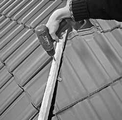 Zamocować na dachówkach zaczepy klamrowe uniwersalne (klamry do dachówek ciętych). Ułożyć dachówki wzdłuż grzbietu zaczepiając druty klamer do wkrętów na łacie grzbietowej.