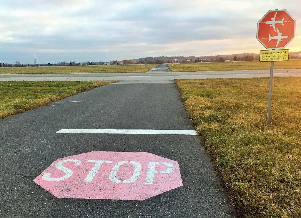 Znak i oznakowanie miejsca oczekiwania na drodze ruchu kołowego przed drogą kołowania.