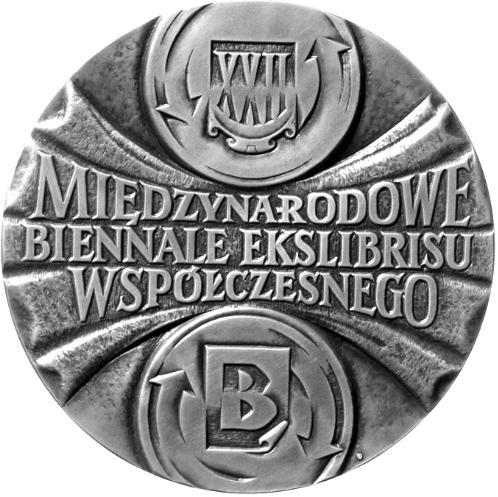 17 Między walcami plik arkuszy papieru, na którym umieszczony jest napis w trzech wierszach: MIĘDZYNARODOWE / BIENNALE EKSLIBRISU / WSPÓŁCZESNEGO Układ arkuszy papieru oraz forma napisu też wyrażają