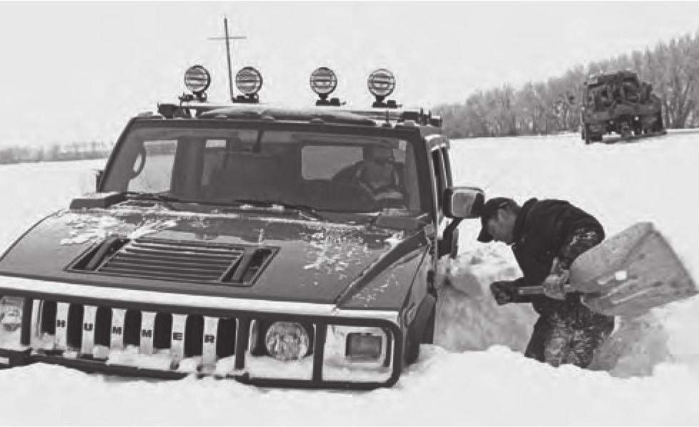 There are two cars in the photo. The car which is in the 1 got stuck in the snow. A man, probably from the other car in the background, is 2 to help dig it out.