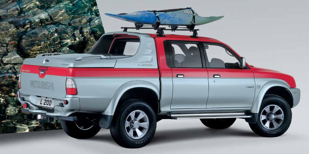 TRANSPORT L200 Double Cab Intense pokazany na zdjęciu ma zamontowany "Fulbox", belki bagażnika z uchwytem na kajak i deskę surfingową, tylny zderzak i hak holownczy.