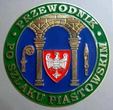 Odznaka Przewodnika po Szlaku Piastowskim przedstawia złotą arkadę łuku romańskiego z kolumnami z kostkowymi głowicami z granatowymi