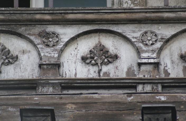 Drewniane elementy dekoracyjne w fasadach kamienic czynszowych z końca XIX i początku XX stulecia ryzalitu falistymi liniami podkreśla wykroje okien I piętra i