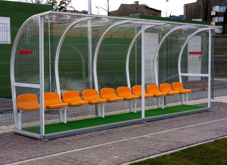 Kabina dla zawodników rezerwowych 12 - osobowa, długość 6 m,wyposażona w siedziska plastikowe z oparciem,w kolorze pomarańczowym Kabina osadzona na ramie