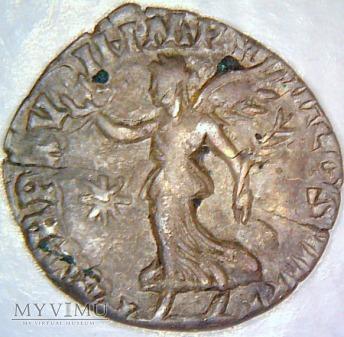 Skrzydlata postać bogini Viktorii z wieńcem w jednej i gałązką oliwną w drugiej dłoni.