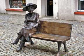 Przedstawia siedzącą na ławeczce naturalnej wielkości postać aktorki.