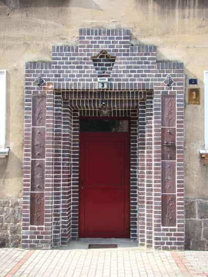 Portal wejściowy budynku przy ul. Jana Boduena de Courtenay 3, wykonany z cegły klinkierowej, ozdobiony płaskorzeźbami. W niszy nad wejściem widoczny postument po zniszczonej rzeźbie (fot. M.