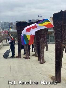 An LGBTQIA2S+ rainbow pride Canada flag hangs from one of the Walking Figures. Pięciu z protestujących stoi pośród żeliwnych rzeźb stworzonych przez polską artystkę Magdalenę Abakanowicz.