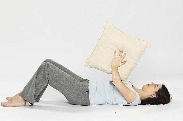 Nadal leżąc w tej samej pozycji co poprzednie ćwiczenie, chwyć poduszkę w dłonie i unieś ją na wysokość klatki piersiowej. Zrób wdech.