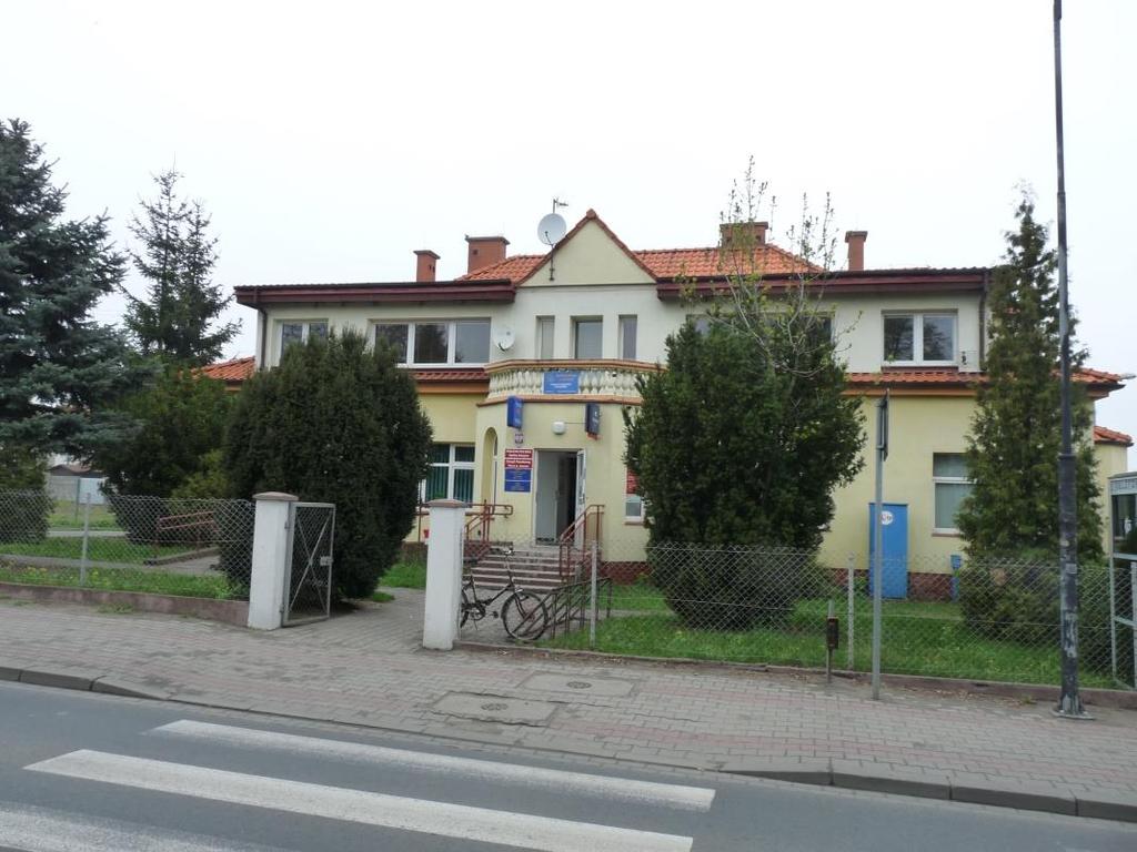 się częściowo zadrzewiony teren zielony (porośnięty trawą), z boku znajduje się ogólnie dostępny parking wydzielony z