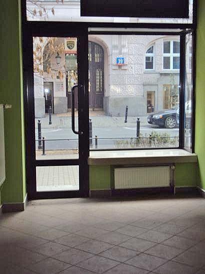 Wejście do lokalu bezpośrednio z ulicy oszklonymi drzwiami, obok duża witryna w formie gabloty