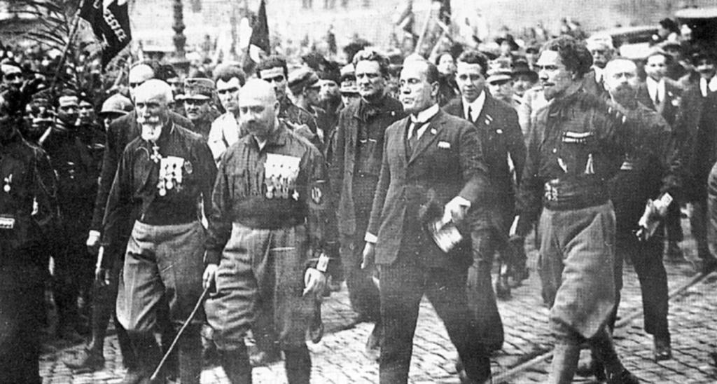 2. Marsz na Rzym. Mussolini ubrany po cywilnemu maszeruje na przodzie, 1919 r. faszystowskimi bojówkami a zwolennikami socjalistów i komunistów. Ranni i zabici byli po obu stronach barykady.
