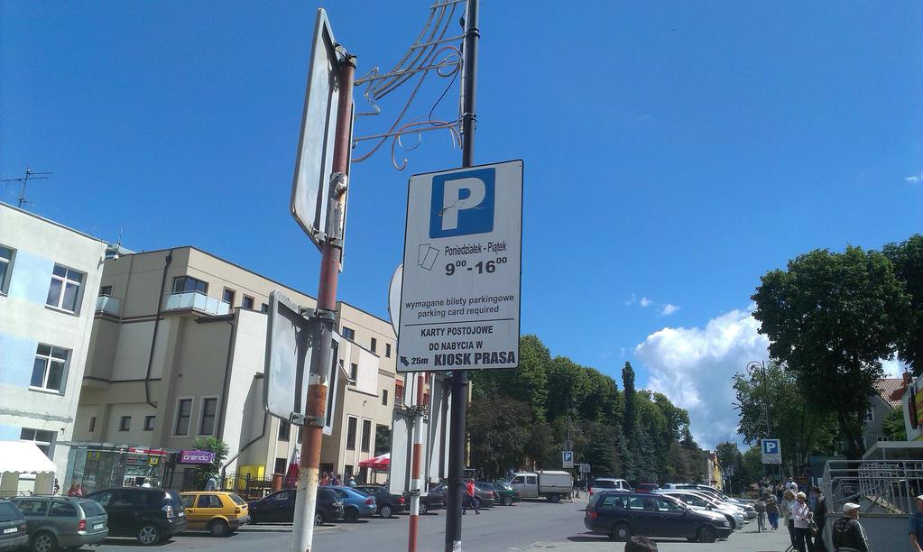 Brak znaków pionowych i poziomych wyznaczających miejsca parkingowe, poustawiane za to jakieś tablica reklamowe zachęcające do kupowania jakichś kart w kiosku z prasą może widokówek z Bartoszyc?