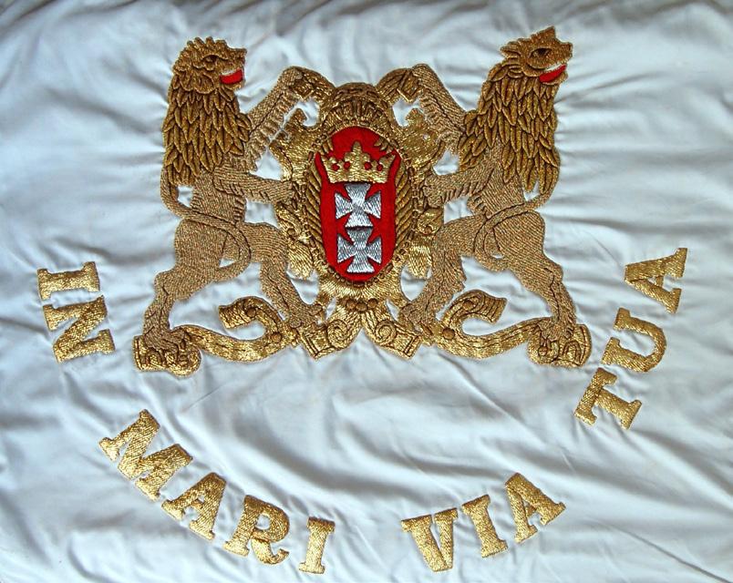 Strona prawa: tło czerwone pośrodku płata sztandaru godło państwowe haftowane srebrnym szychem i bajorkiem.