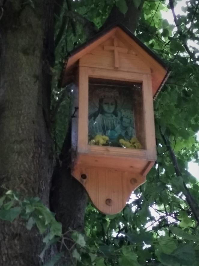 RATÓWKI Przy leśnej drodze prowadzącej Olszyn do Jodłówki Tuchowskiej na drzewie przybita jest drewniana szafkowa kapliczka z rzeźbionym w drewnie wizerunkiem
