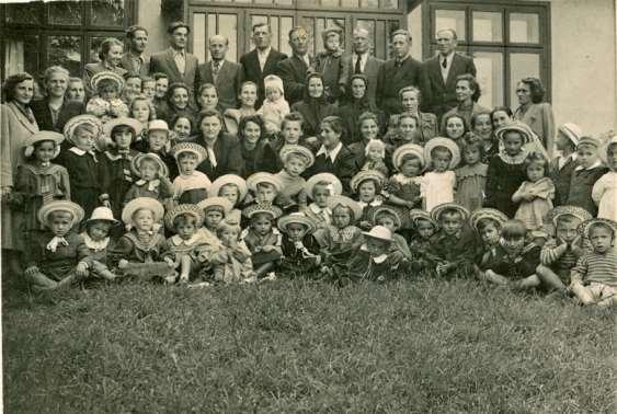 3 Zdjęcie 1 Rok 1952 (około). Dzieci 3-6 letnie z przedszkola z wychowawczyniami i rodzicami oraz babciami. W tle budynek fotografa Leona Sokołowskiego. Autor zdjęcia Leon Sokołowski.