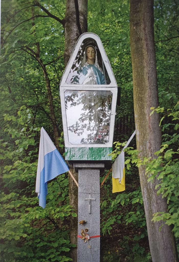 Kapliczka Matki Bożej, umieszczona na betonowym słupie, znajduje się z prawej strony górnej części cmentarza przy kościele w Łaziskach.