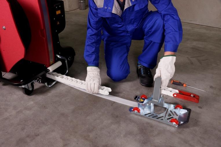 Zawiń mechanizm prowadzący do góry jak pokazano na rysunku i za pomocą śrubokręta odkręć obie śruby na taśmie